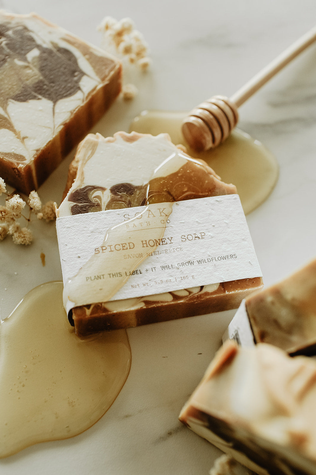 Spiced honey soap with a label on a marble surface with honey and a honey dipper.