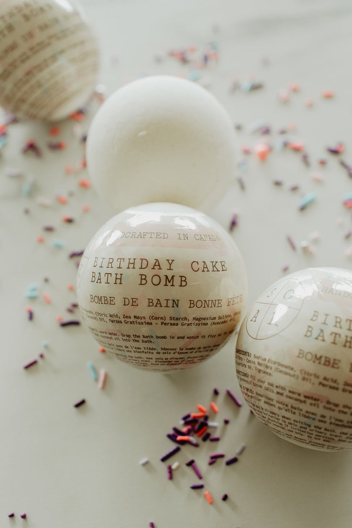 Birthday cake bath bomb with text on a white surface with colorful sprinkles