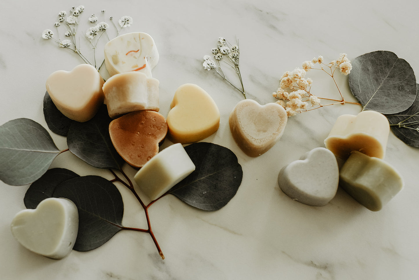 Heart-shaped soaps on a marble surface with leaves and flowers