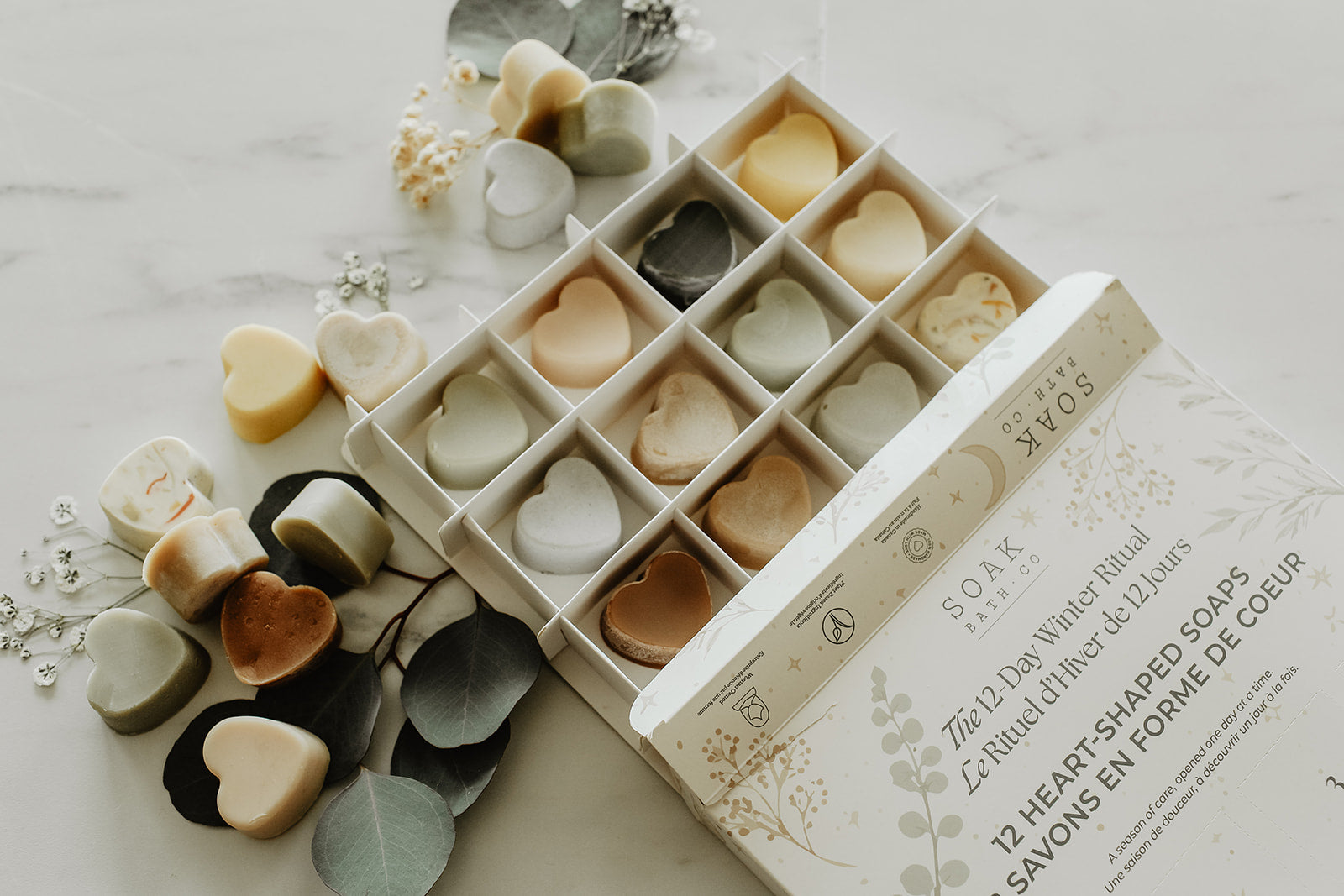Heart-shaped soaps in a decorative box on a light surface with flowers.