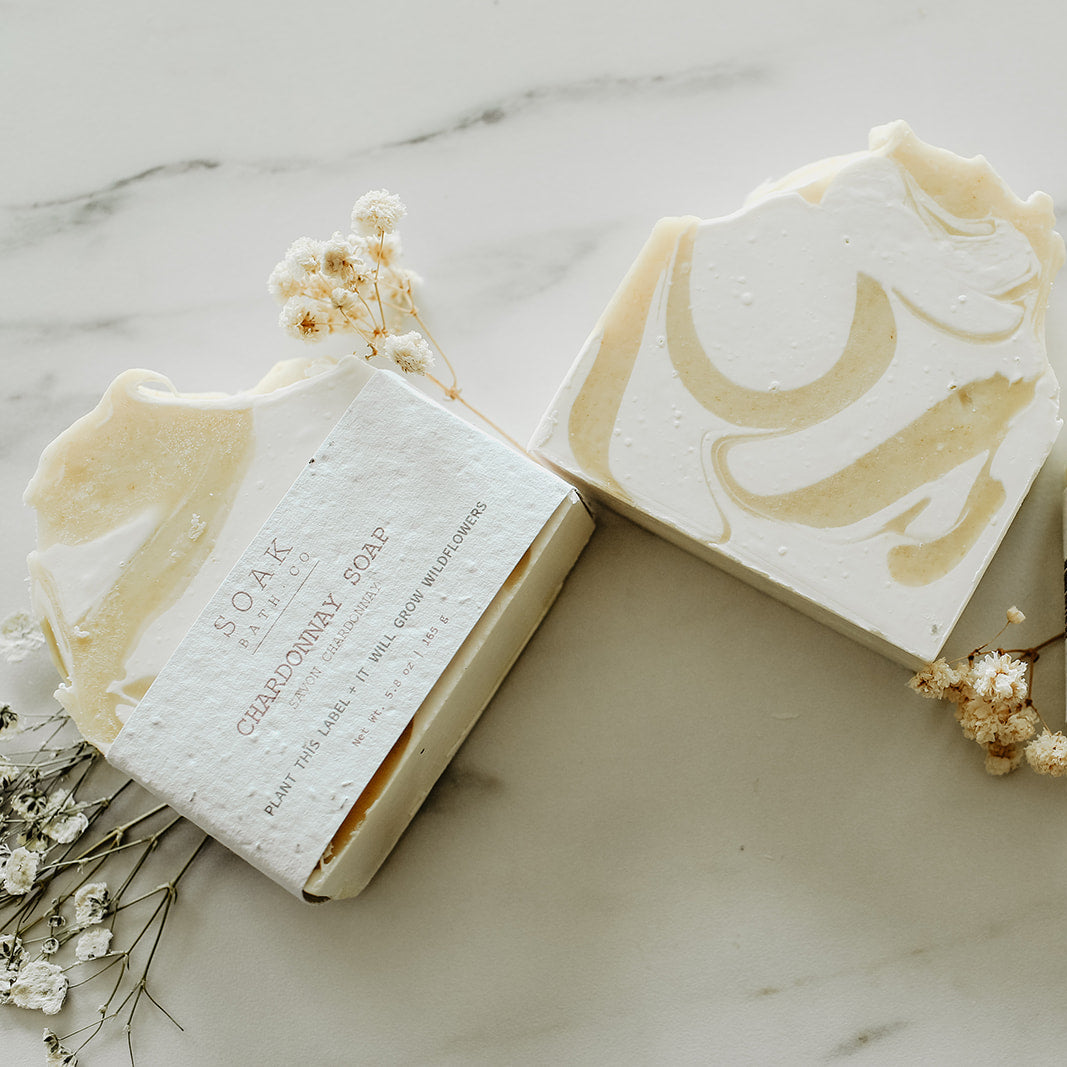 Three bars of soap with branding on a marble surface with small flowers.