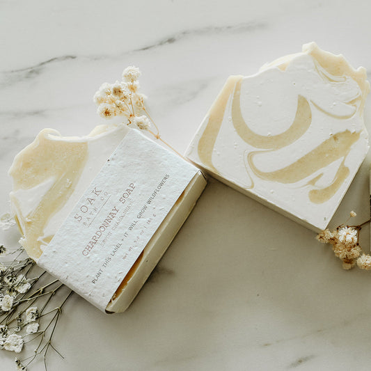 Three bars of soap with branding on a marble surface with small flowers.