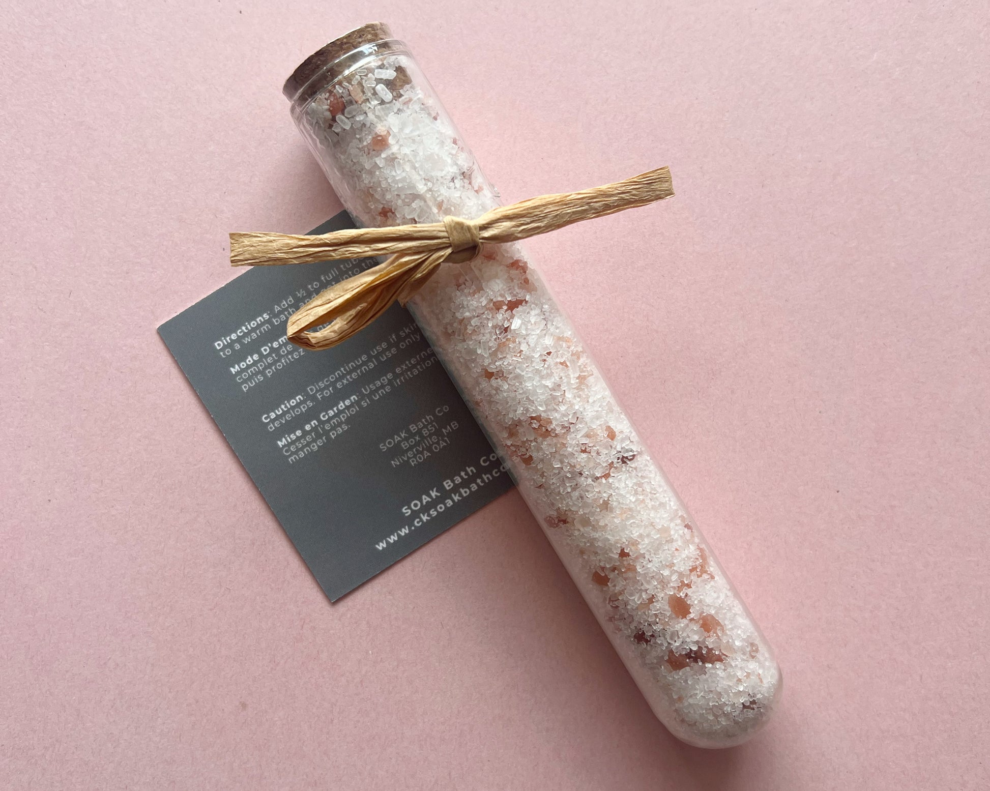 Bottle of bath salts with a wooden stick on a pink background