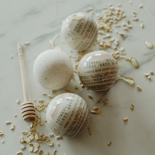 Bath bombs with newspaper labels on a marble surface with oats and a honey dipper.