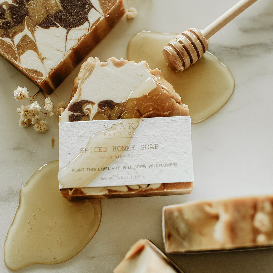Decorative soap bars with a honeycomb and honey drizzle on a marble surface.