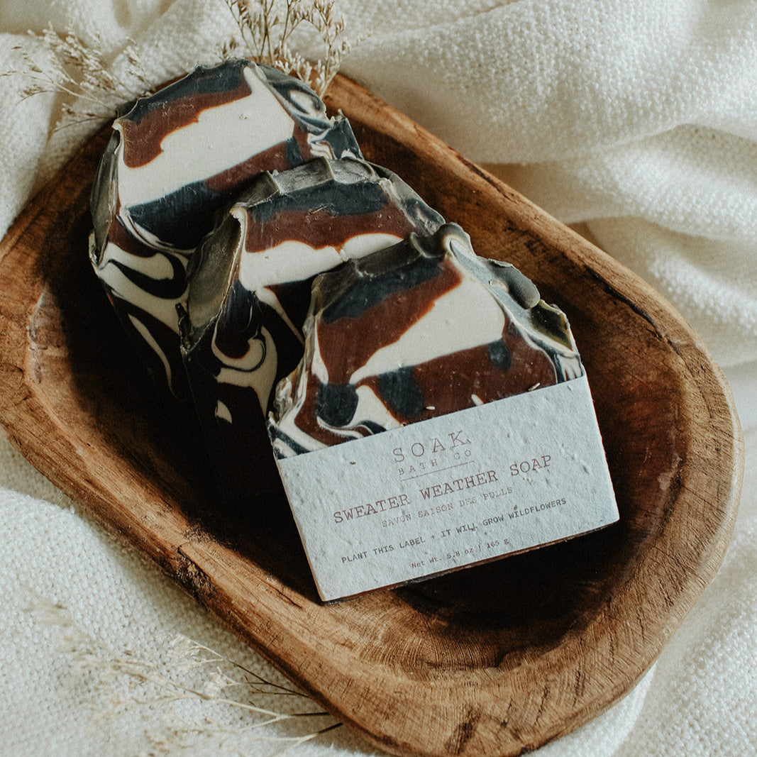 Marbled Sweater Weather soap bar with a label on a wooden dish over a white fabric background