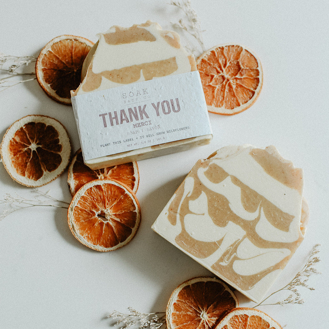 Two bars of soap with decorative packaging surrounded by dried orange slices on a light background