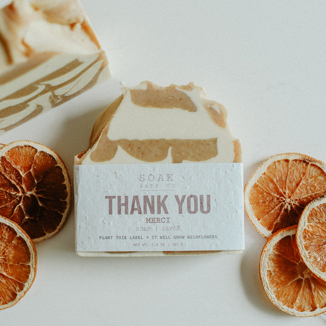 Bar of soap with a 'Thank You' message surrounded by dried orange slices on a light background