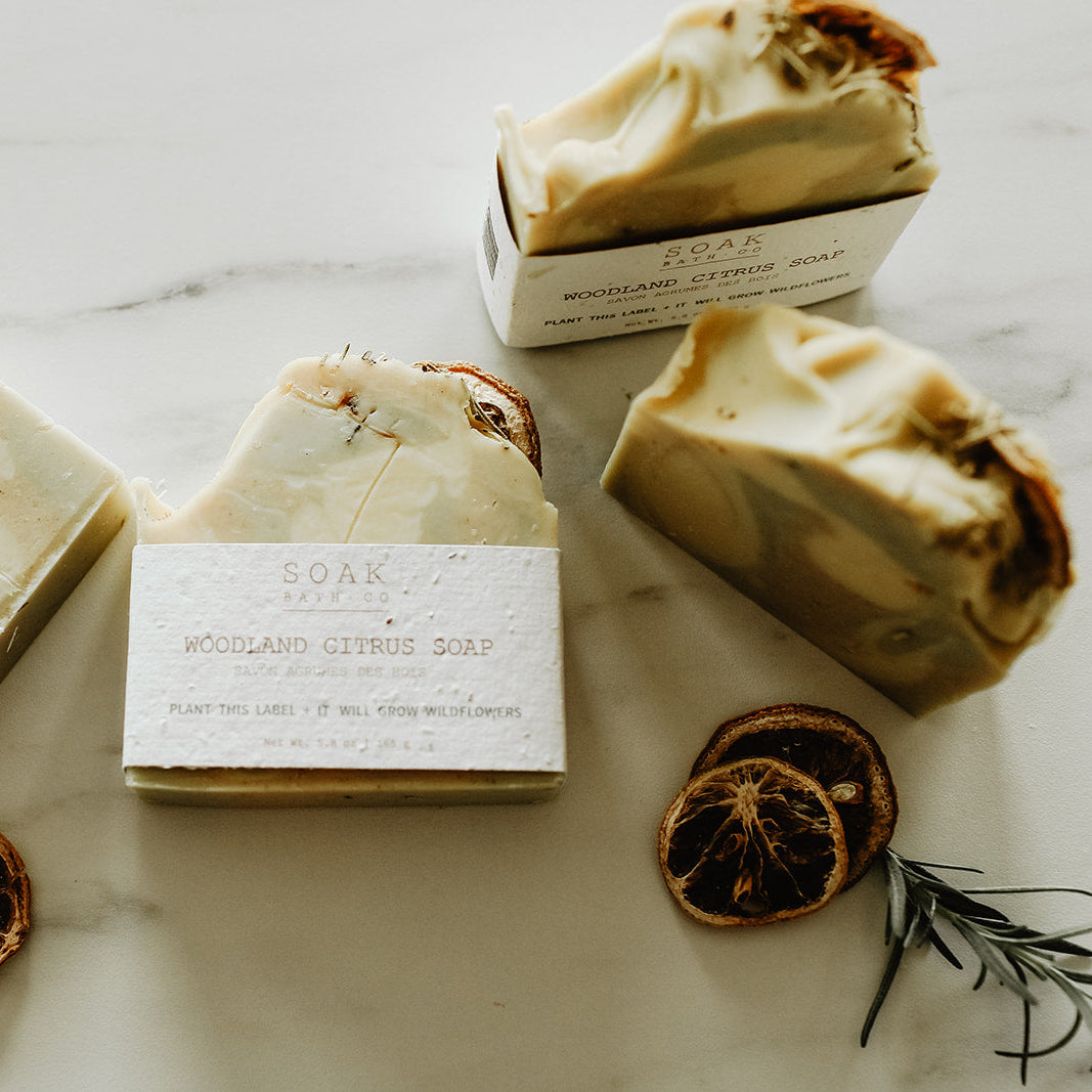 Bar of soap with packaging on a marble surface with dried oranges and rosemary.